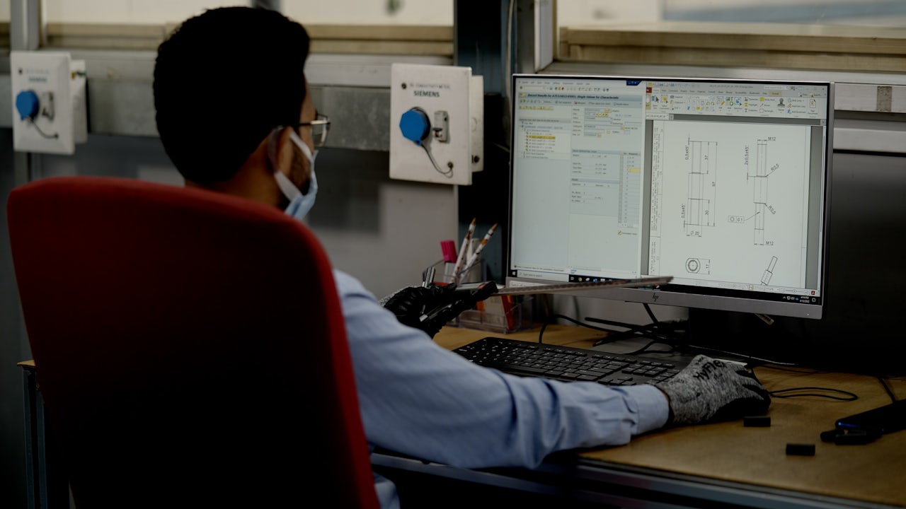 Person in black shirt standing against white wall, holding a dark object with blurred background.