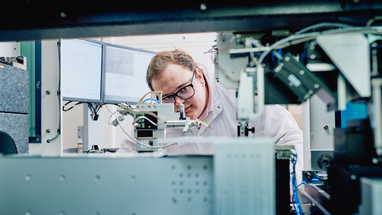 Person in black shirt standing against white wall, holding a dark object with blurred background.