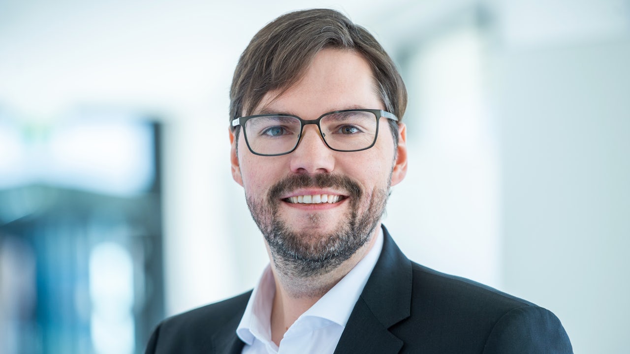 The image shows a person standing in front of a large, colorful mural with a mix of abstract and realistic elements.