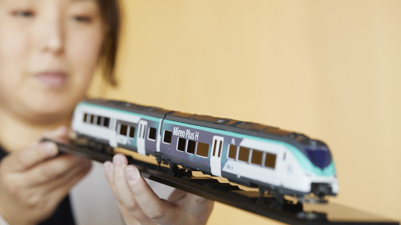 Woman in black dress with tied-back hair posing against blurred white wall, gazing to the right