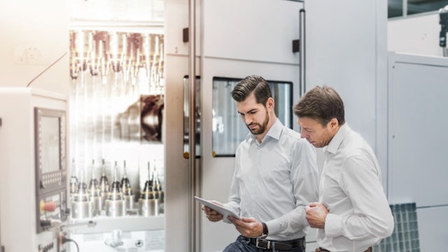 Two men standing and looking at information on a tablet device.