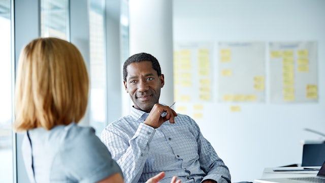 Two colleagues (man and a woman) sitting in an office having a conversation.