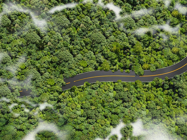 A car driving on a road surrounded by greenery and a clear sky.