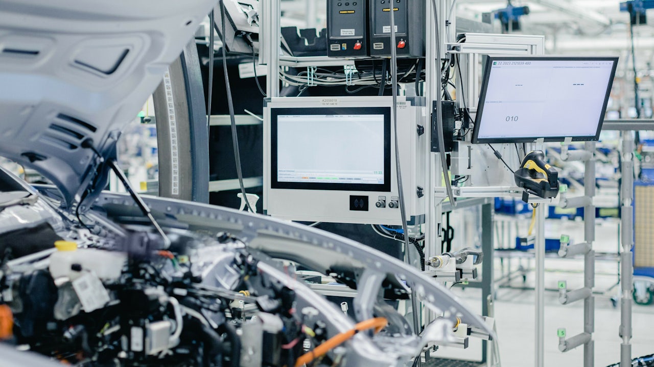 A close-up of the engine of a vehicle with diagnostic equipment and a computer behind it. 