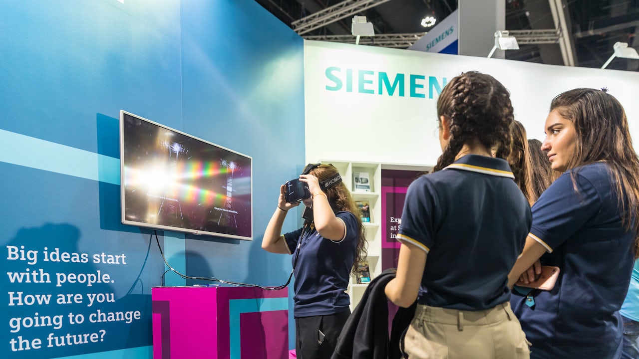 A person stands in front of a large, colorful mural featuring abstract shapes and bright colors, in an urban setting.