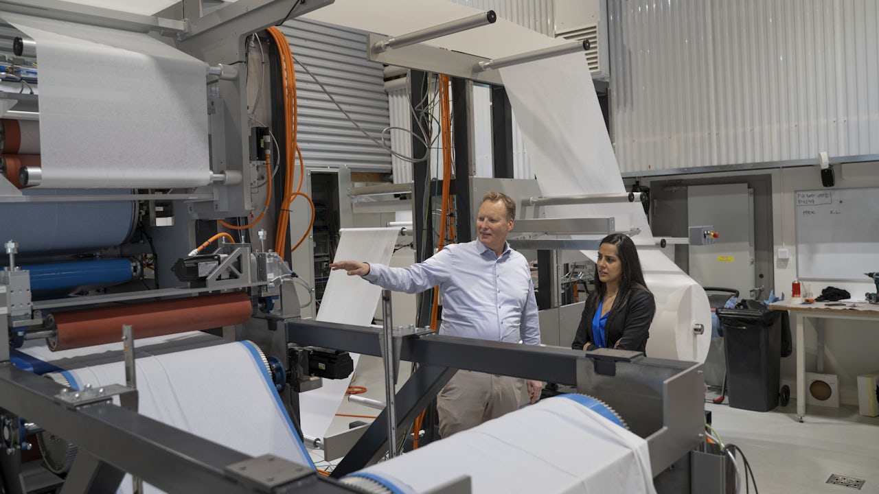 A person is standing in front of a large screen displaying a graph with a blue line.