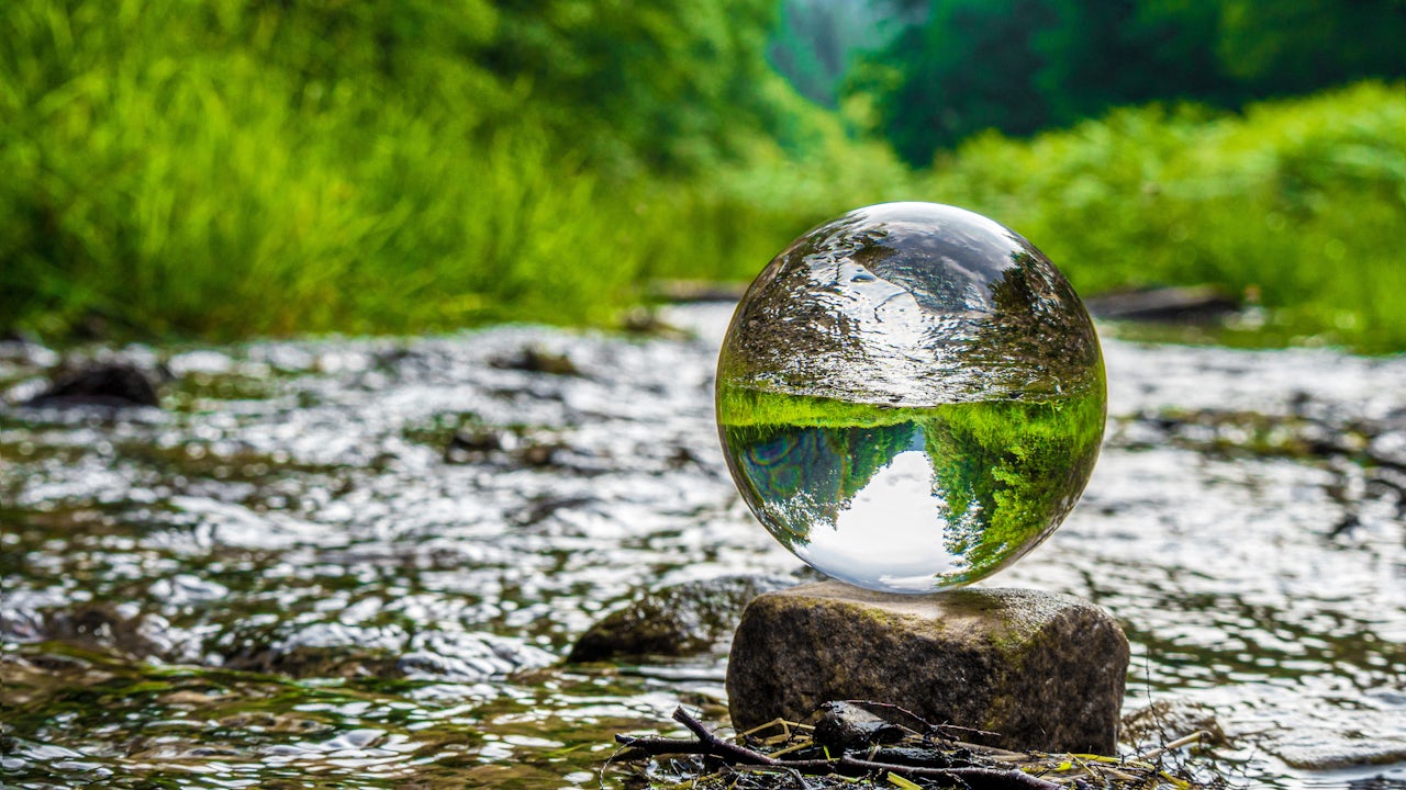 A reflective sphere magnifies the fresh water stream and green foliage that are in the background.