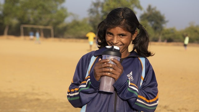 Girl on a playground smiling and drinking