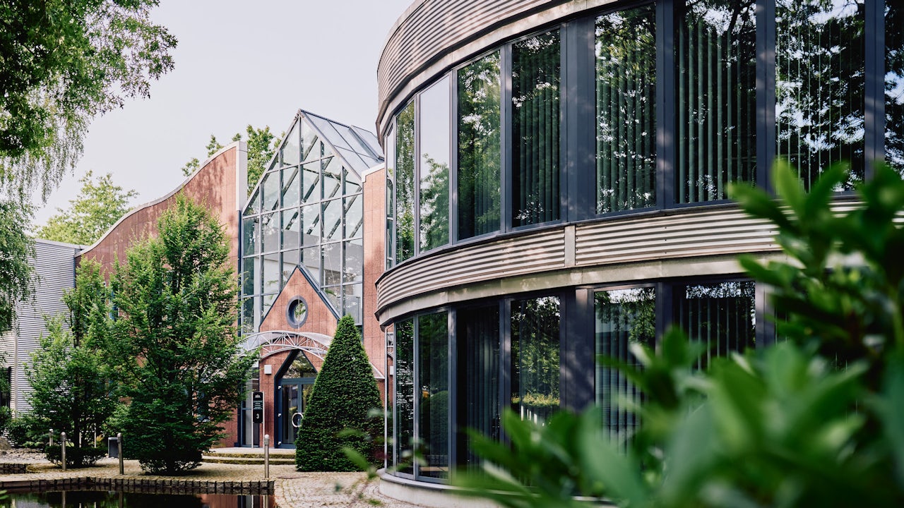 Person in black shirt standing against white wall, holding a dark object with blurred background.