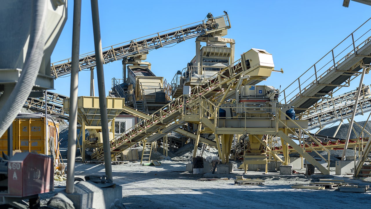 A person is standing in front of a white wall, wearing a black shirt and a black hat.
