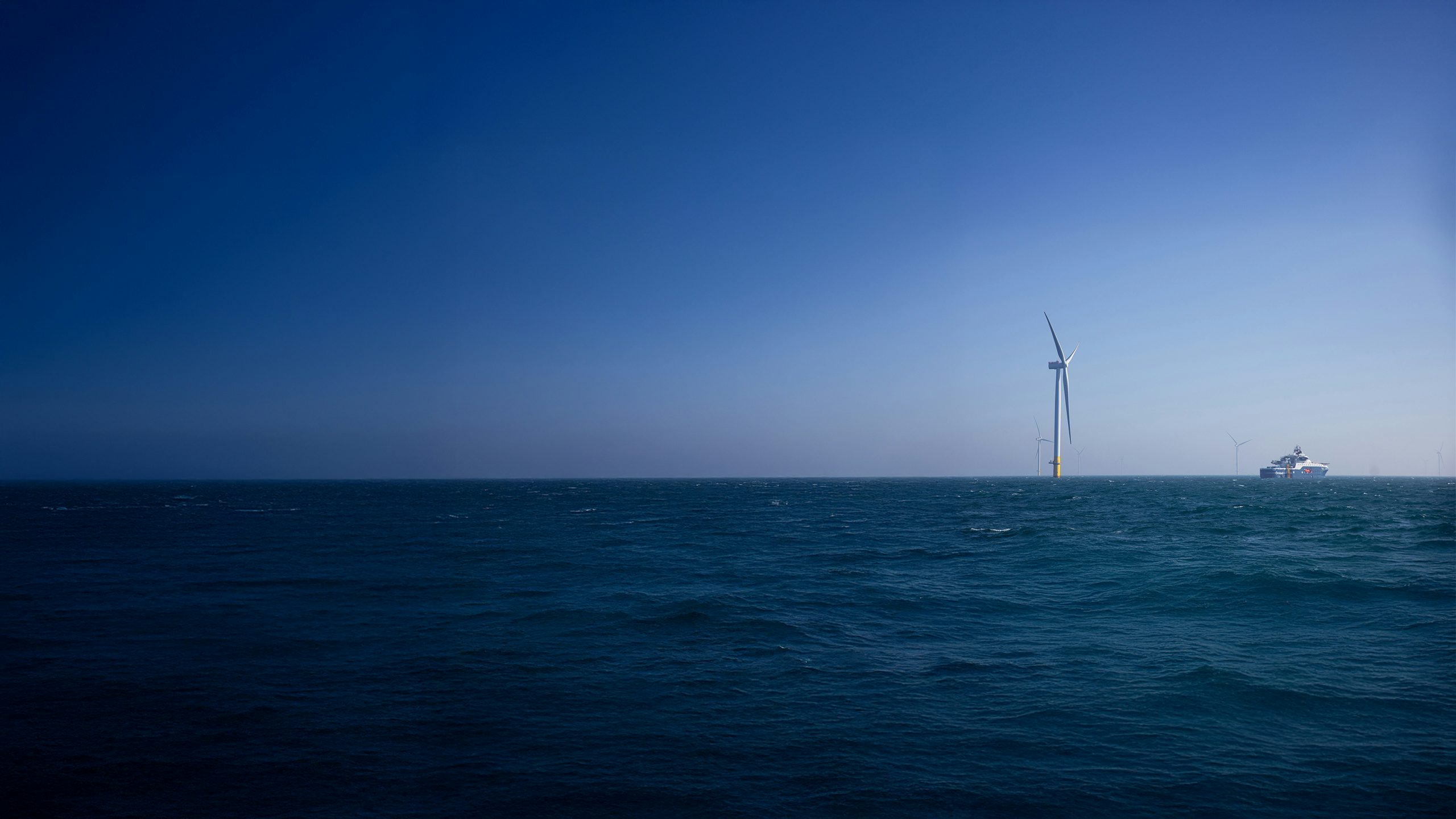 A large ship sails near a windmill that has been built in the ocean.