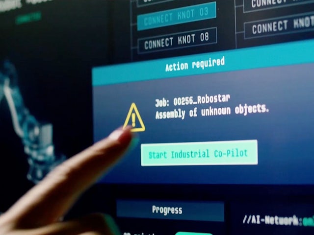 Person in black shirt standing against white wall, holding a dark object with blurred background.