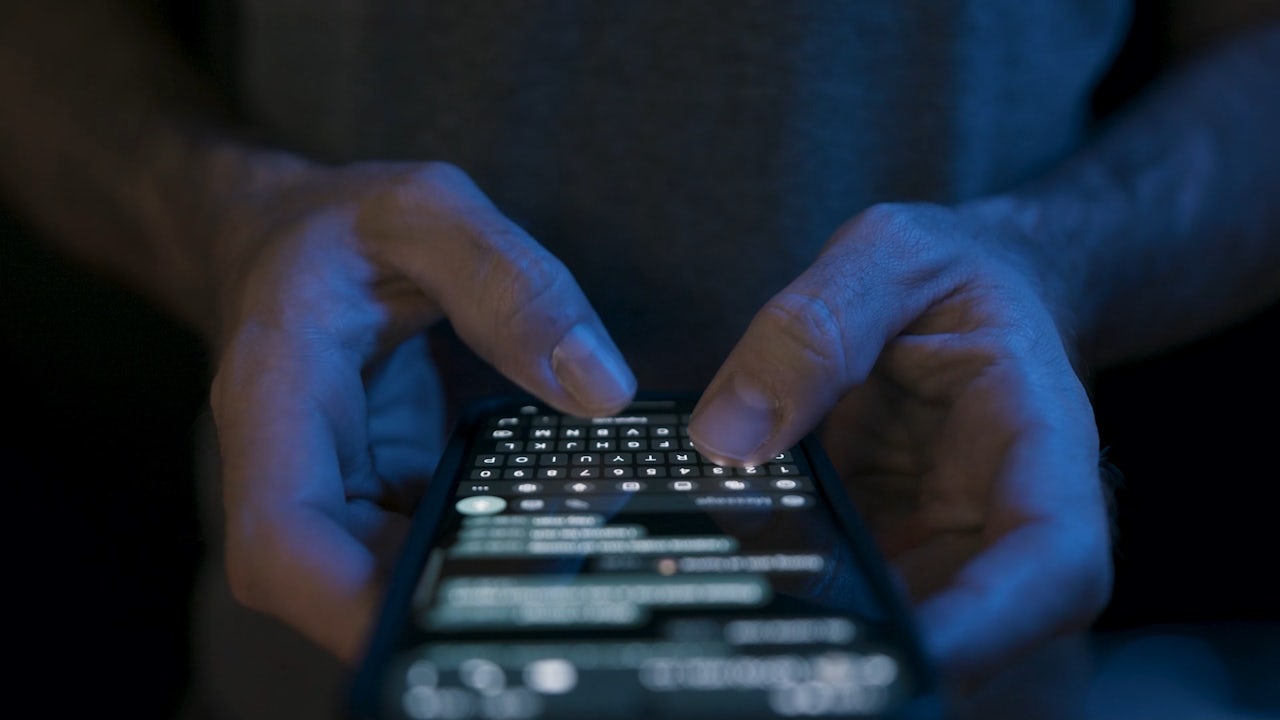 The image shows a person wearing a blue shirt and a white hat standing in front of a white wall.
