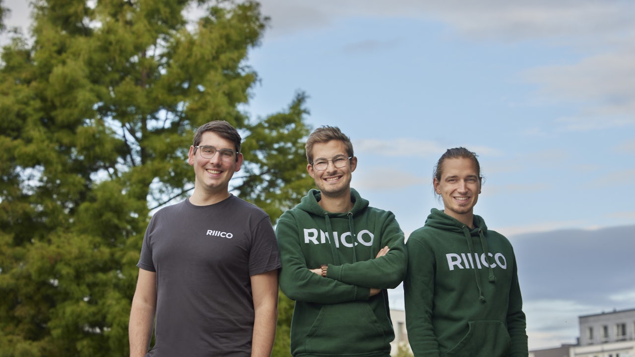 A person stands in front of a building with a large window, holding a piece of paper.