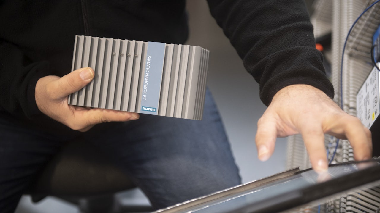 A person holds a SIMATIC Nanobox PC while tapping a screen.