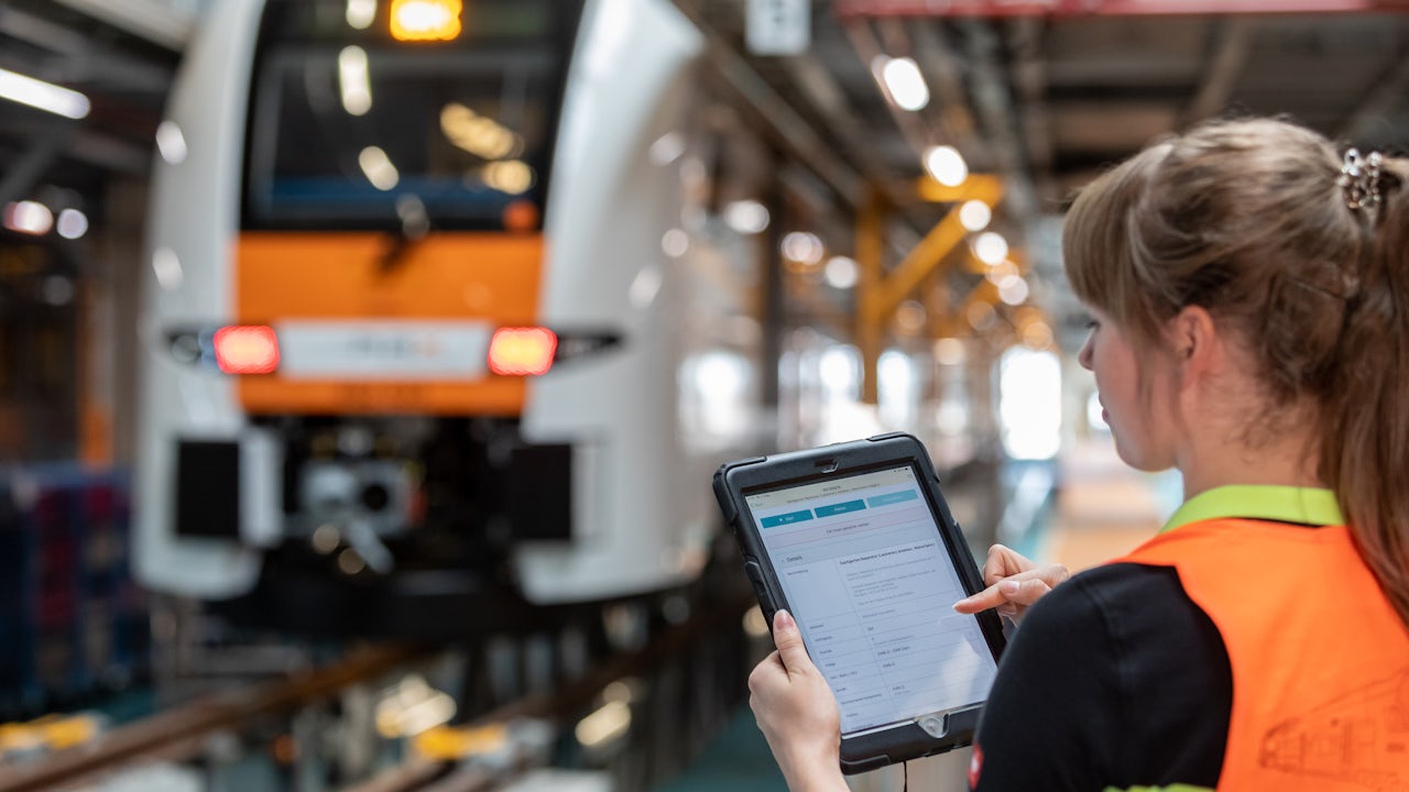 A person is standing in front of a large building with a blue sky and clouds in the background.