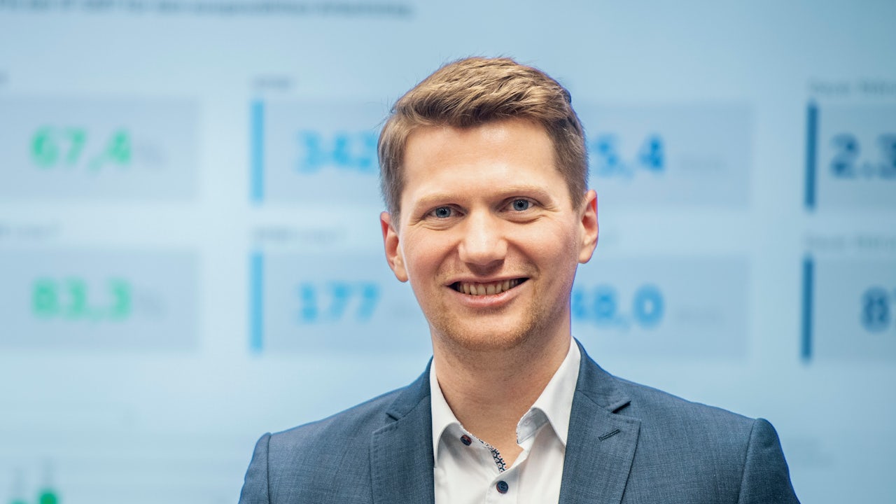 A person in a suit and tie is standing in front of a large screen displaying a graph.
