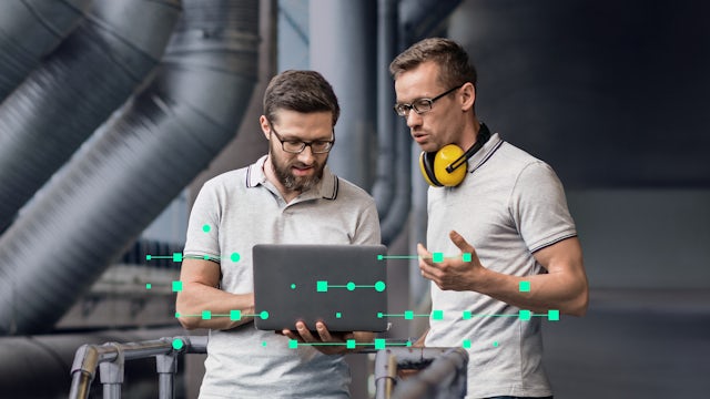 Two male engineers in an industrial setting, one holding a laptop, discussing data represented by green digital overlays.