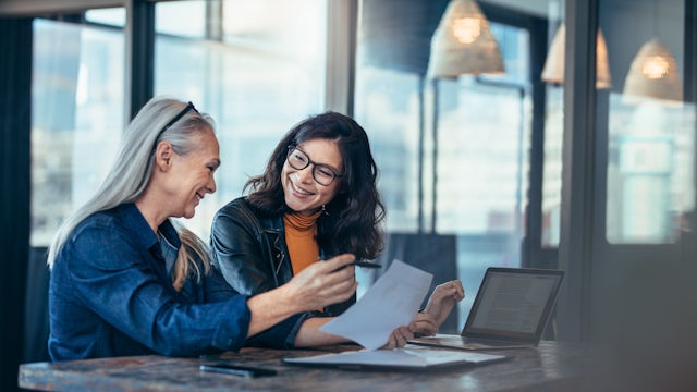 Two colleagues sitting in an office having a conversation and smiling.