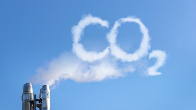 A smoke stack from a manufacturing plant with white smoke coming out the top, in the shape of the CO2.