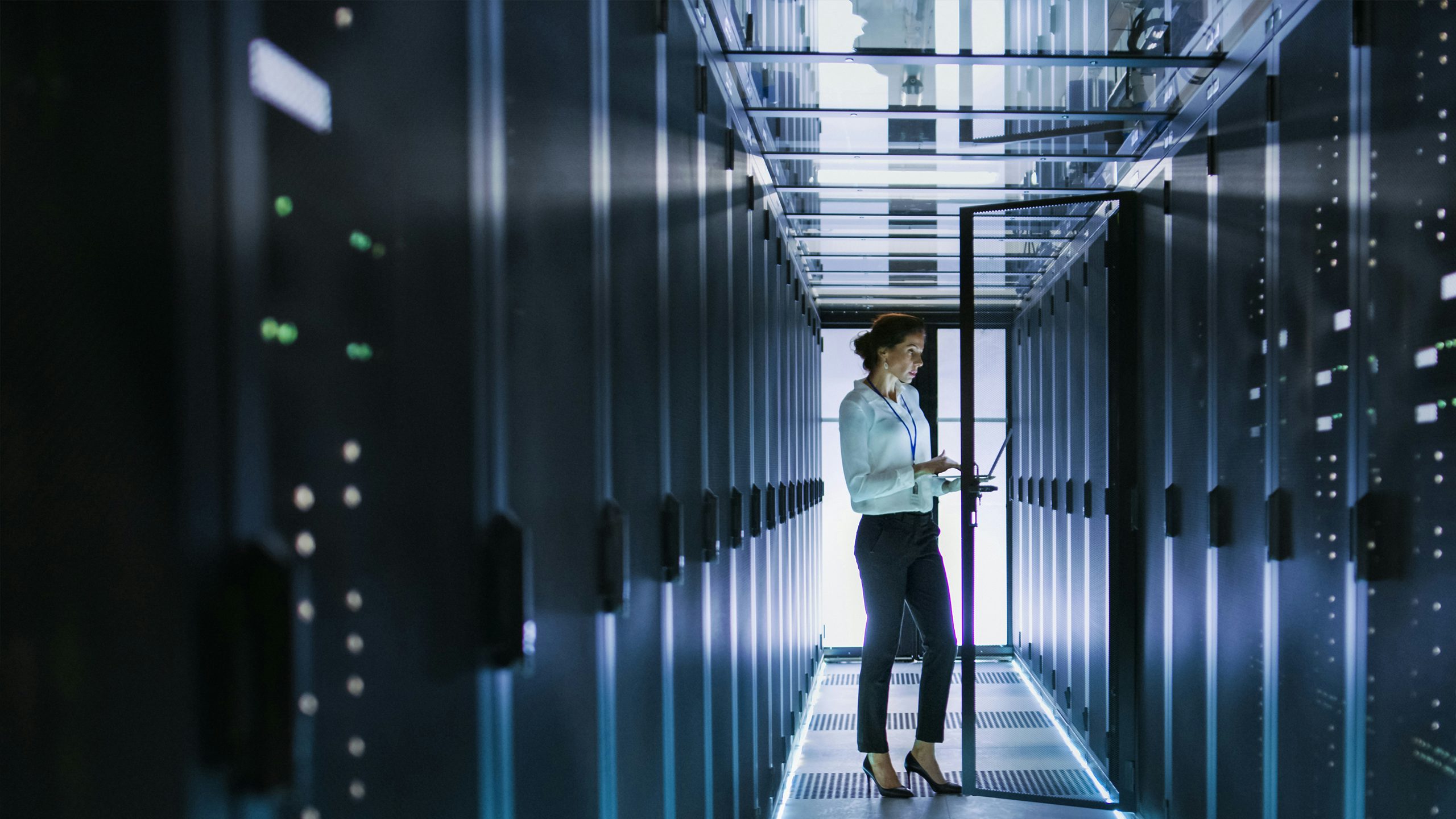 A woman standing in a data center with rows of servers and networking equipment in a modern facility.
