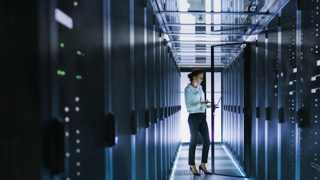 A woman standing in a data center with rows of servers and networking equipment in a modern facility.