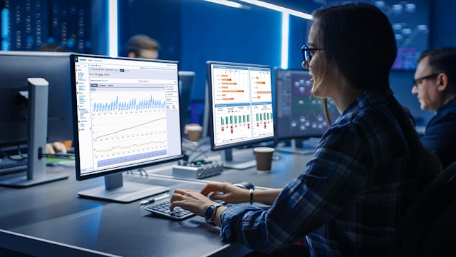A professional woman wearing glasses in a low-lit office working at a computer.