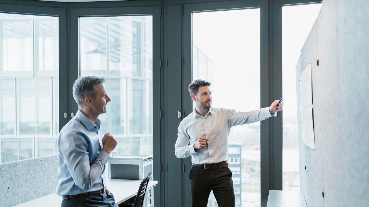 Two business men having a discussion in front of a board.