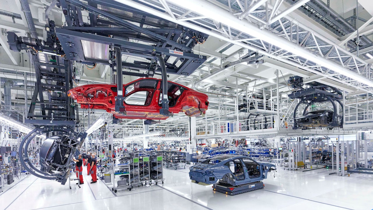 The frame of a red Audi hangs in an automotive plant.