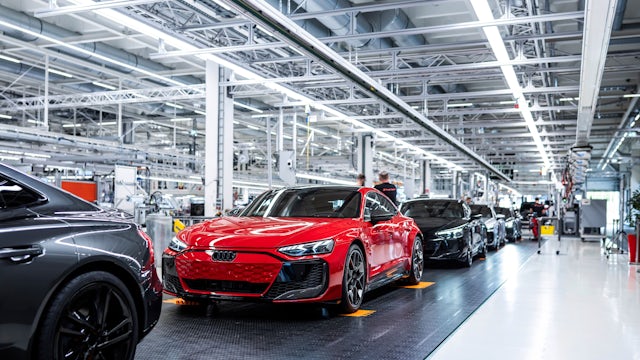 A person is standing in front of a white wall with a blue and white logo.