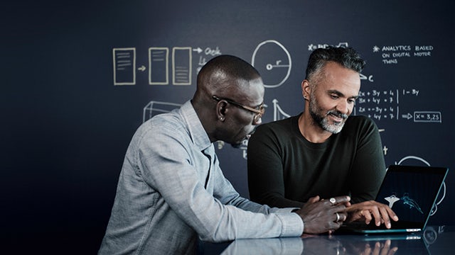 A person in a blue shirt and mask is standing in front of a blue wall with a white sign.