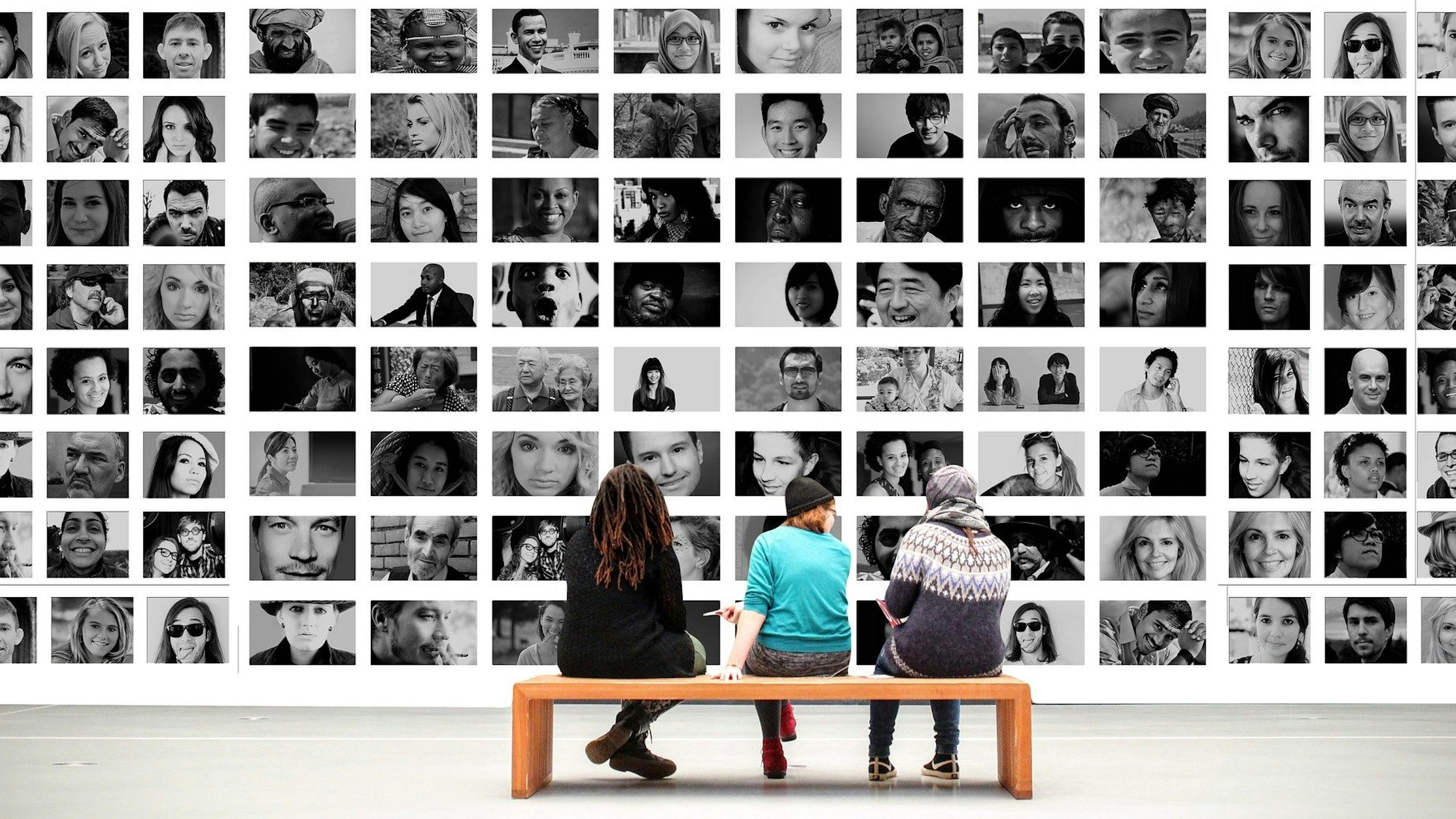 People sitting on a bench looking a wall of photographs.