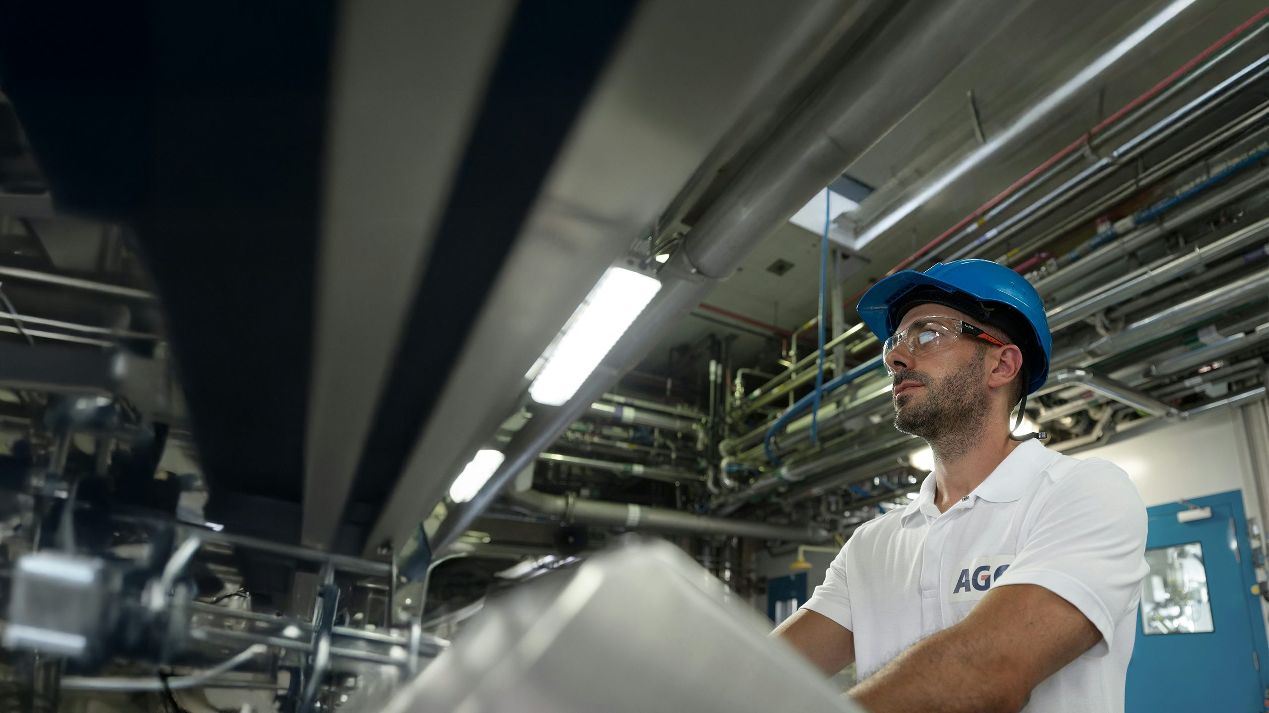 Man in blue hard hat and safety glasses in a factory.