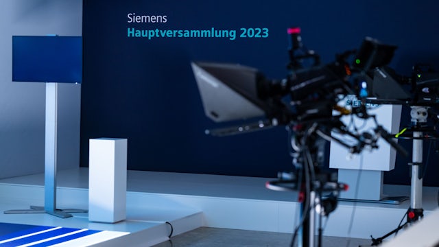 A group of people are gathered in a conference room for an annual shareholder meeting.