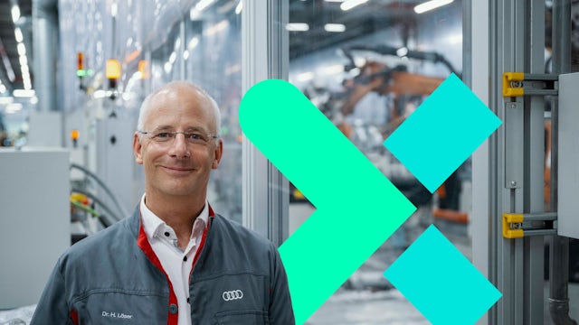 Dr. Henning Löser, Audi, stands on a factory floor with robots working in the background.