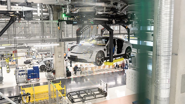 A Porsche car is displayed in a showroom with a spotlight on it.