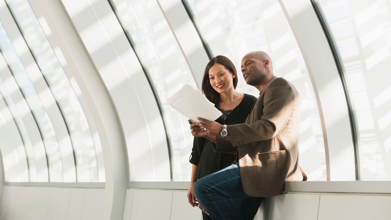 Two professionals sitting in a hallway reviewing documents.