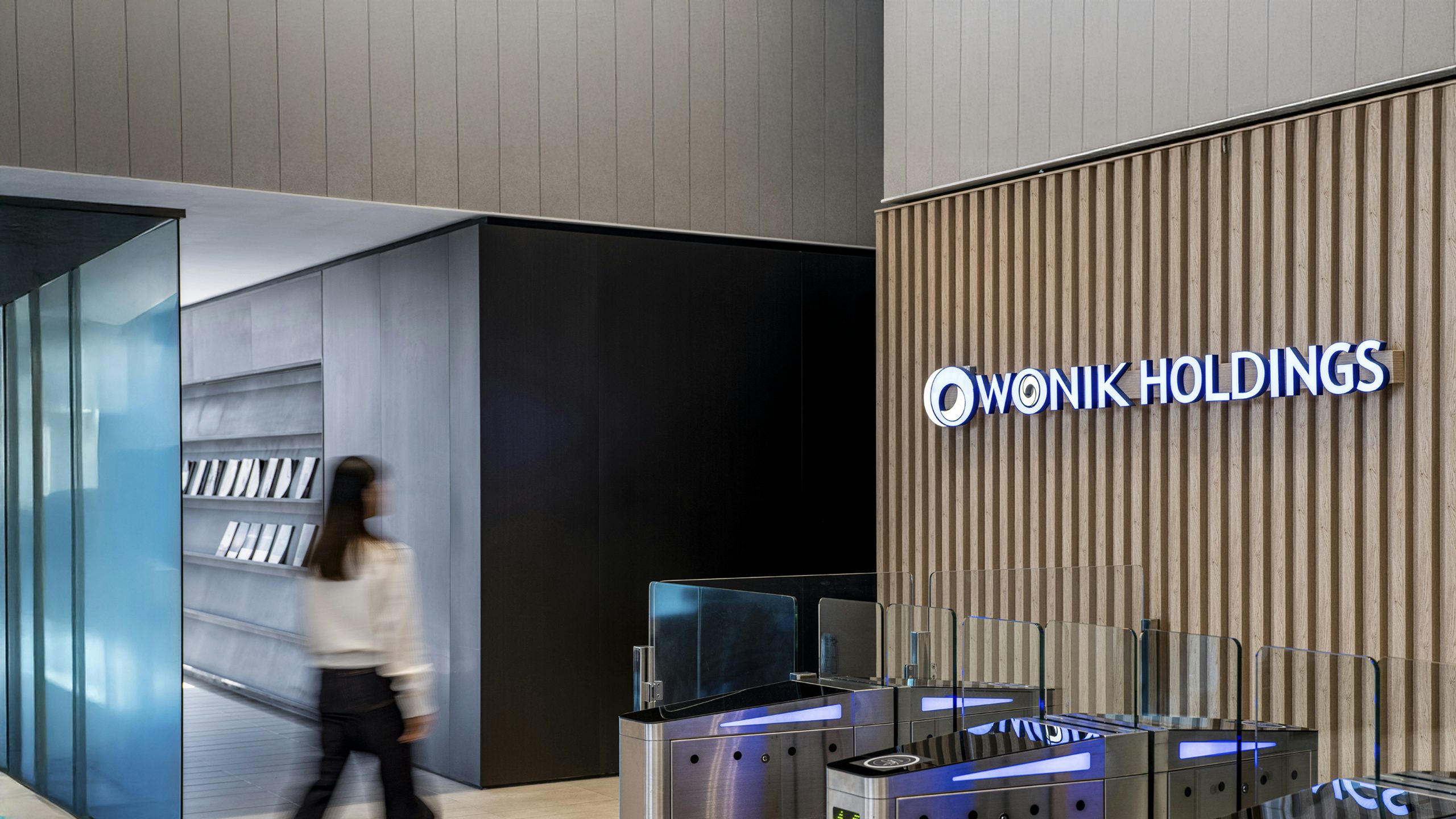 A person is standing in front of a building with a large window, wearing a white shirt and a black jacket.