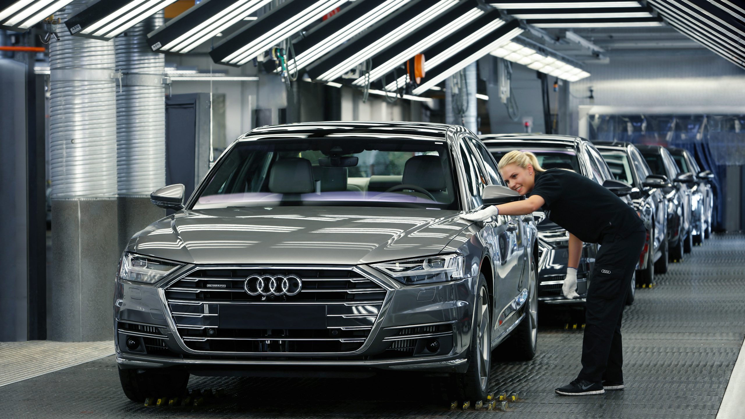 A woman on the Audi assembly line inspecting the alignment of the body panels on a finished car.