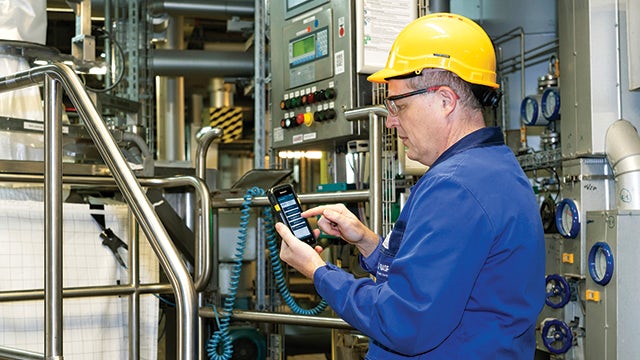Scientist in lab coat and safety glasses examining a beaker with blue liquid