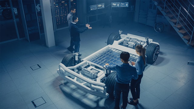 Digital rendering of four people in a clean manufacturing facility discussing the chassis of an electric vehicle