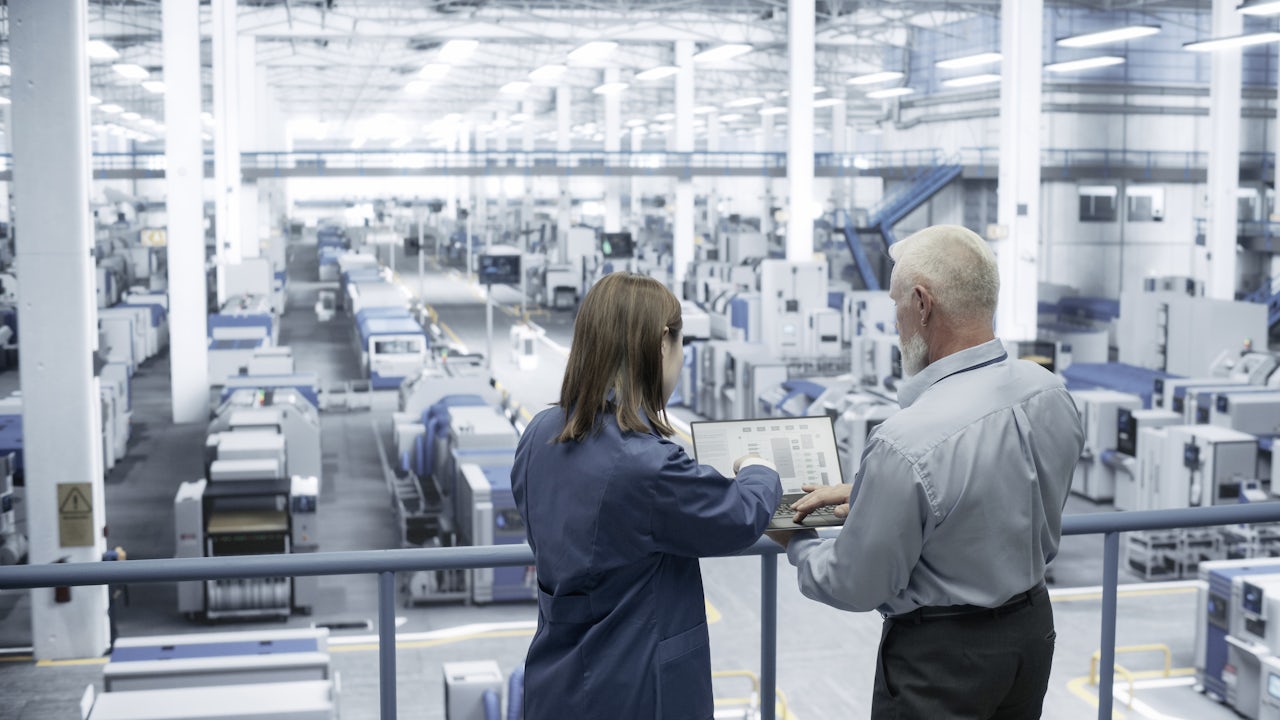 Two workers in a factory looking at a control panel.