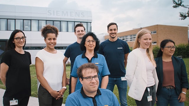 A group of people in a meeting room, smiling and looking engaged in a discussion.