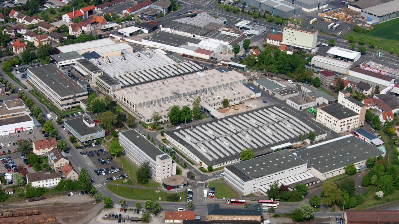 Aerial view of a large circular arena or stadium with a distinctive roof structure surrounded by parking lots and roads.