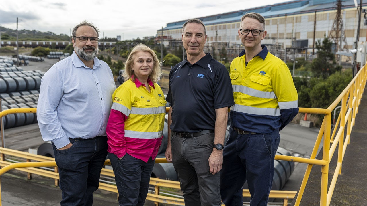 Members of the BlueScope team, standing outside the factory on a catwalk.