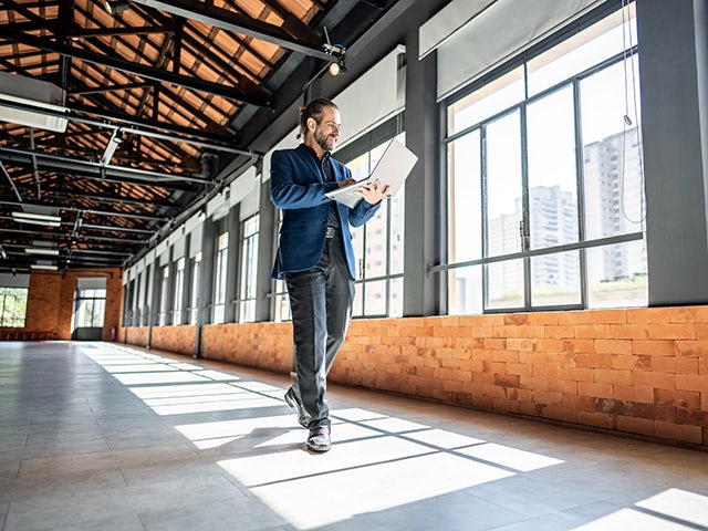 Mature businessman walking and using laptop in an empty commercial real estate property.