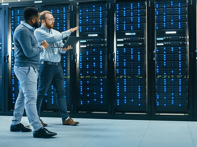 IT technicians with a laptop talking in a data center while walking next to server racks.