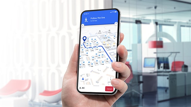 Person holding a mobile phone in an office with the Pointr app showing directions.