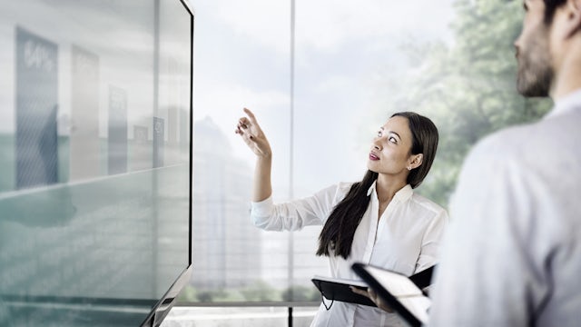 Businessman and businesswoman discussing finance in front of a screen with a graph.