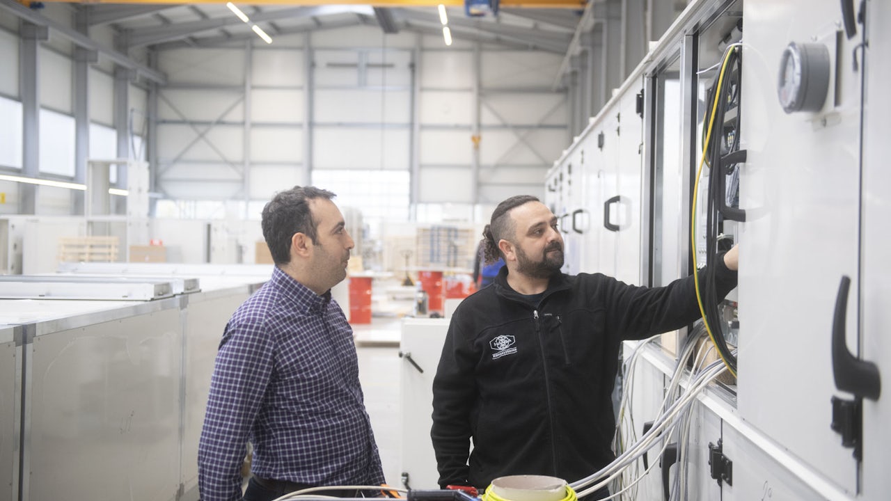 Two men look at ventilation equipment for an indoor pool.